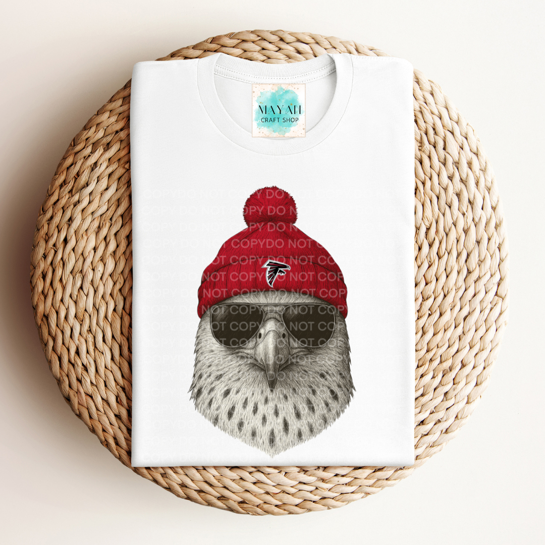 White t-shirt with a bird wearing a red beanie on a woven surface