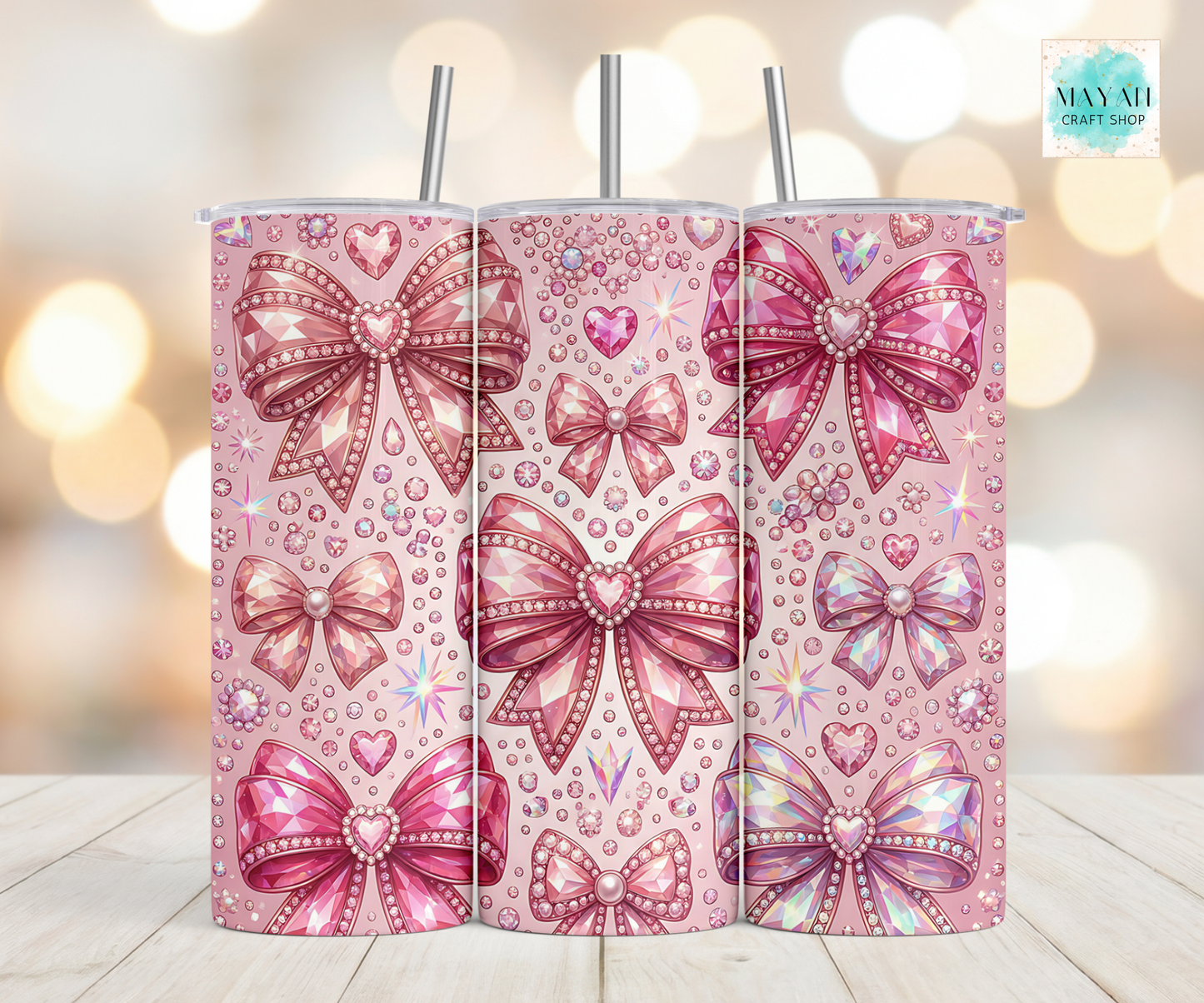 Three pink tumbler with bow designs on a wooden surface with a blurred background.