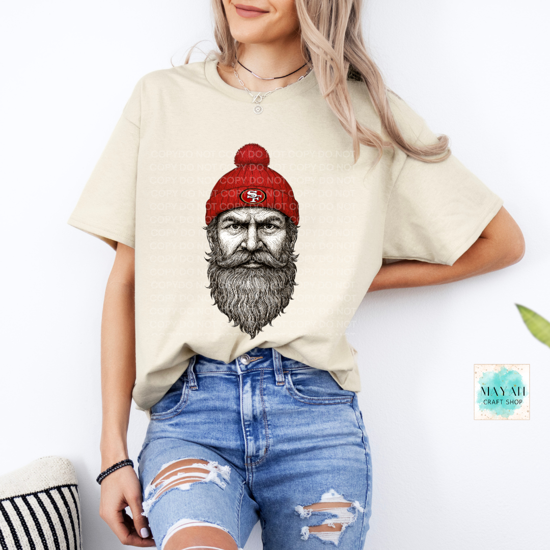 Person wearing a beige t-shirt with a graphic of a bearded man in a red beanie, standing against a white background.