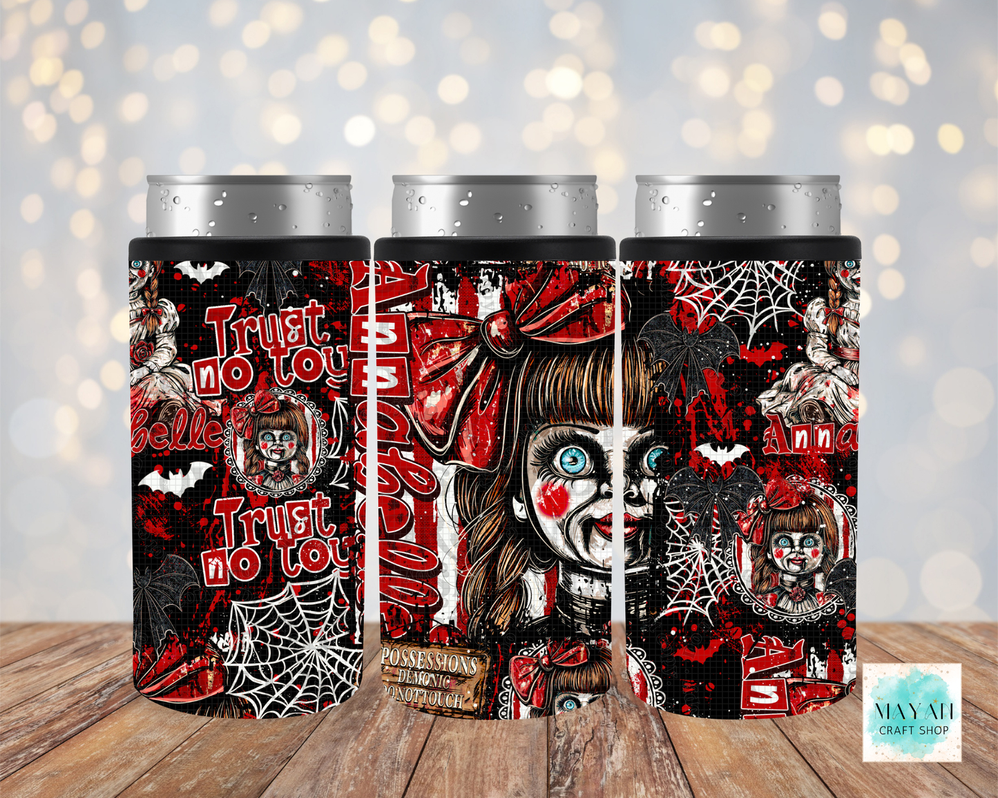 Three slim can coolers with silver aluminum can tops, featuring a horror-themed design with red, black, and white graphics, displayed on a wooden surface against a blurred bokeh background.