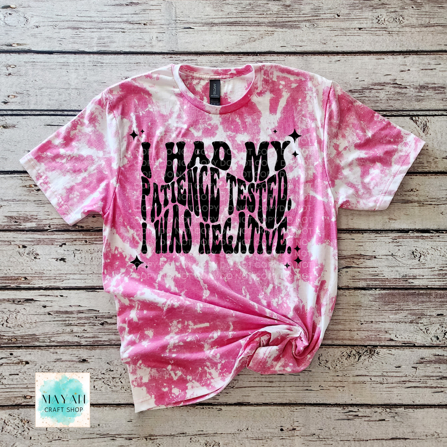 Pink tie-dye t-shirt with black text on a wooden surface, featuring the brand 'Mayan Craft Shop'.