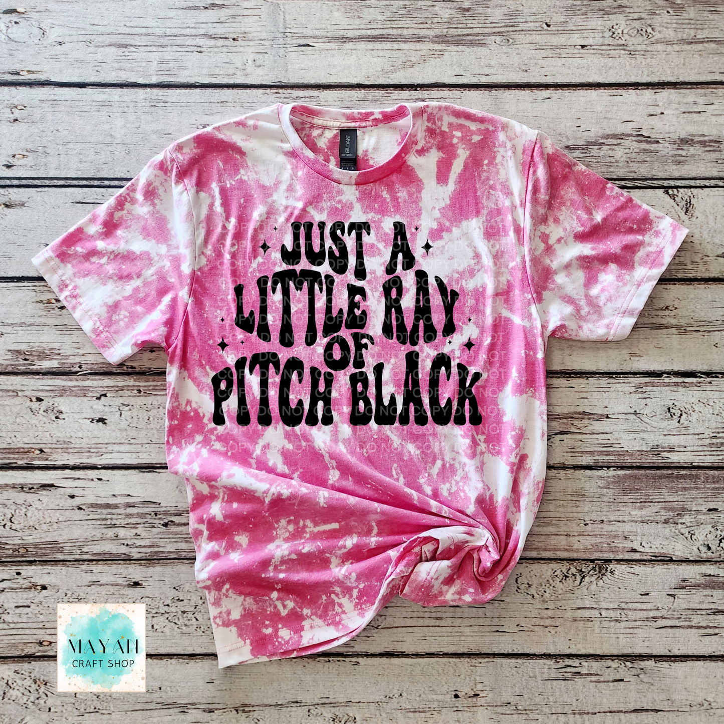 Pink tie-dye t-shirt with black text on a wooden surface, featuring the brand 'Mayan Craft Shop'.