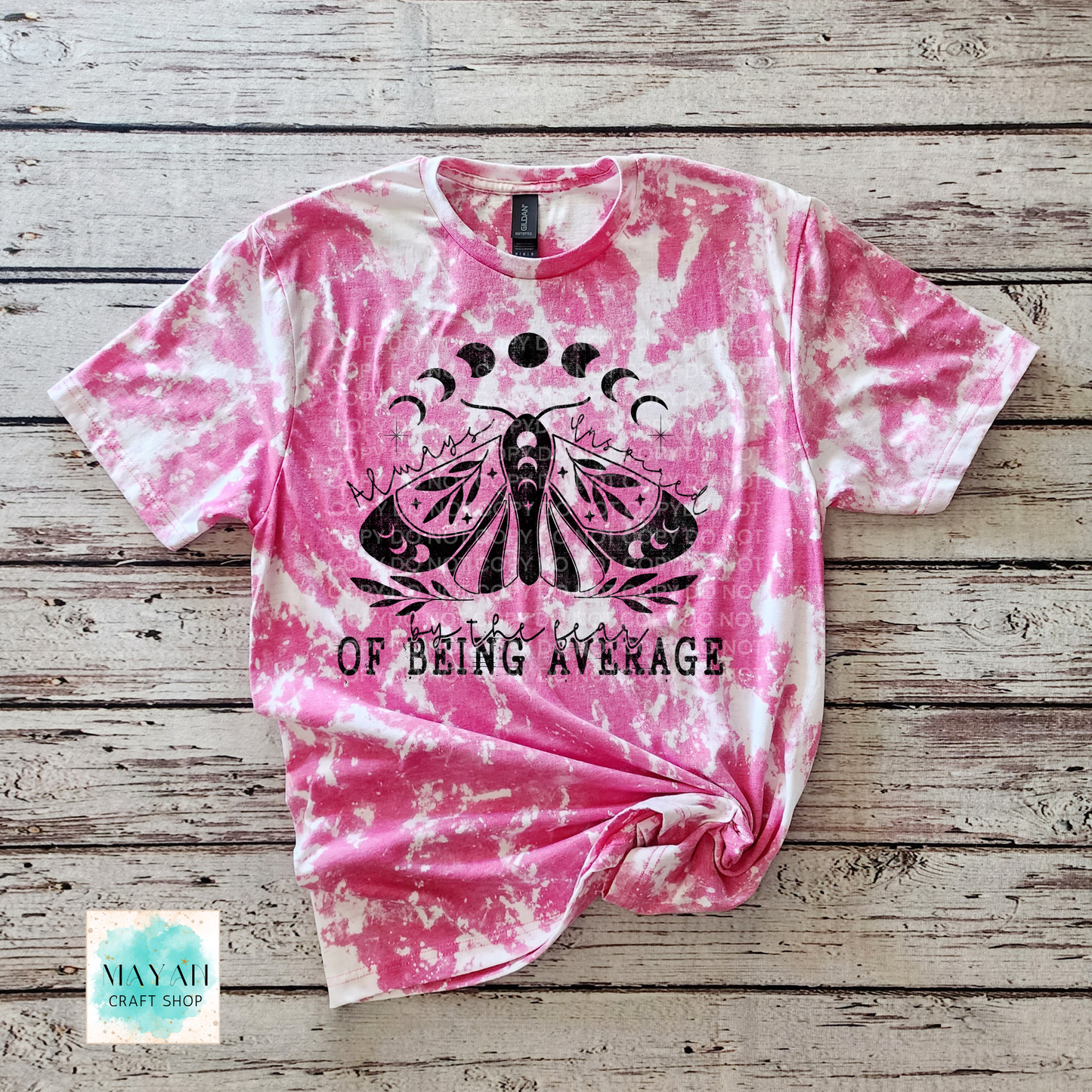 Pink tie-dye t-shirt with black moth graphic and text on a wooden surface, 'Mayan Craft Shop'.