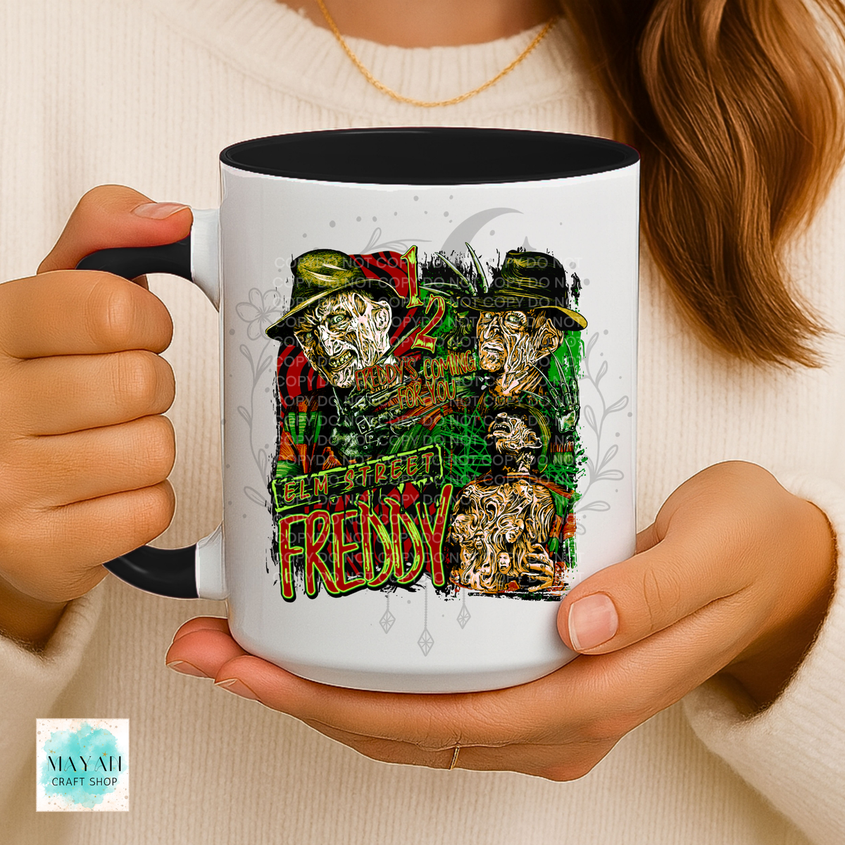 A person holds a white ceramic mug with a black handle and interior. The mug features a colorful graphic print of faces with a text in large stylized letters.