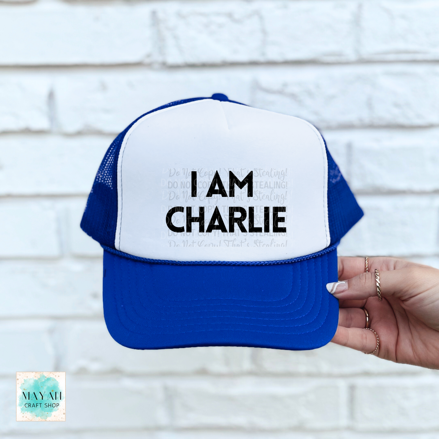 Blue and white cap with 'I AM CHARLIE' text held against a light brick wall.