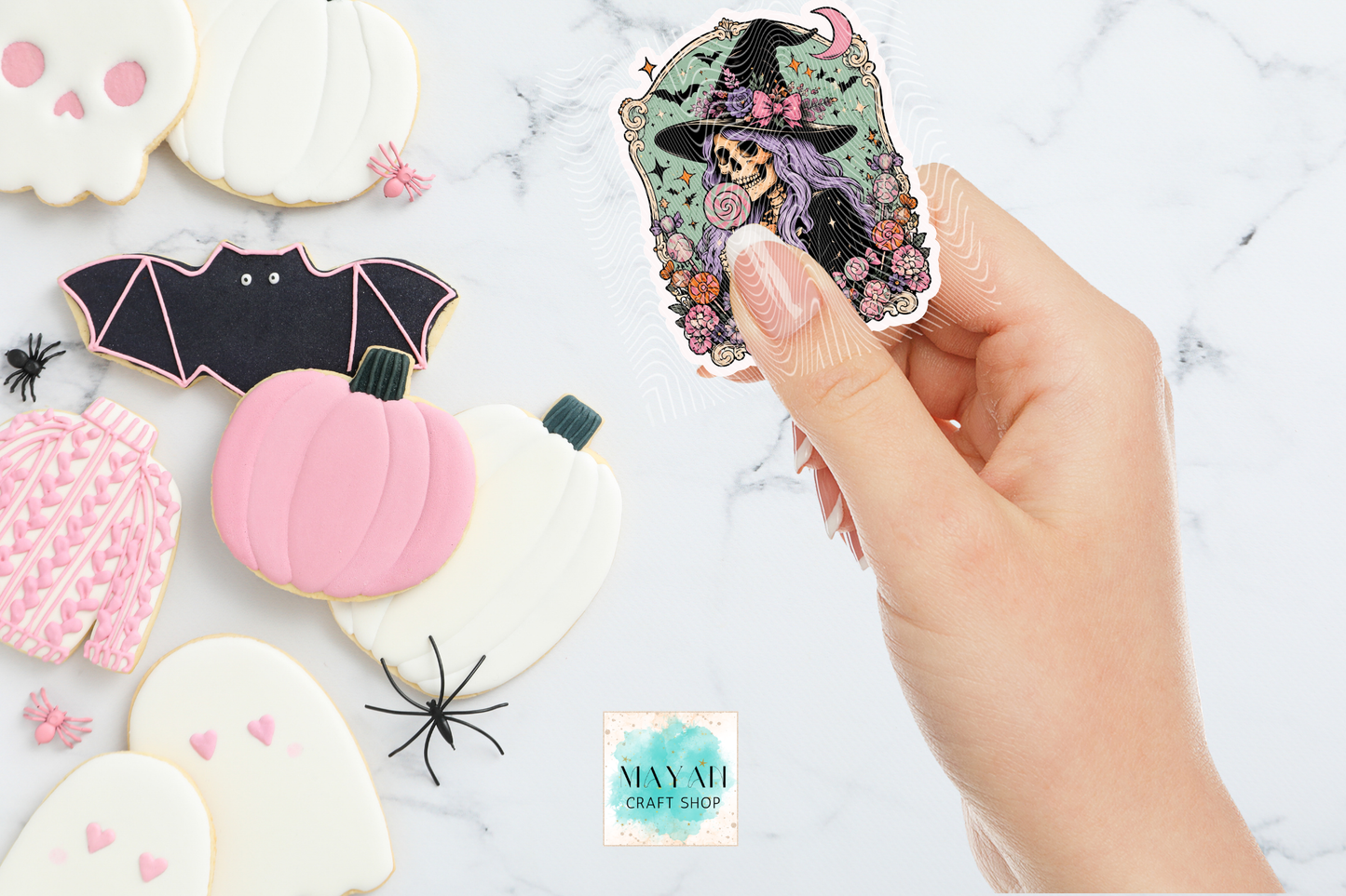 Hand holding a Halloween sticker with other decorated cookies on a marble surface.