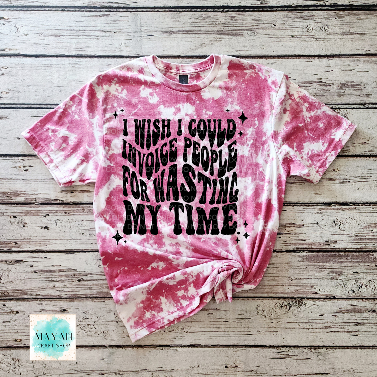 Pink tie-dye t-shirt with black text on a wooden surface, featuring the brand 'Mayan Craft Shop'.