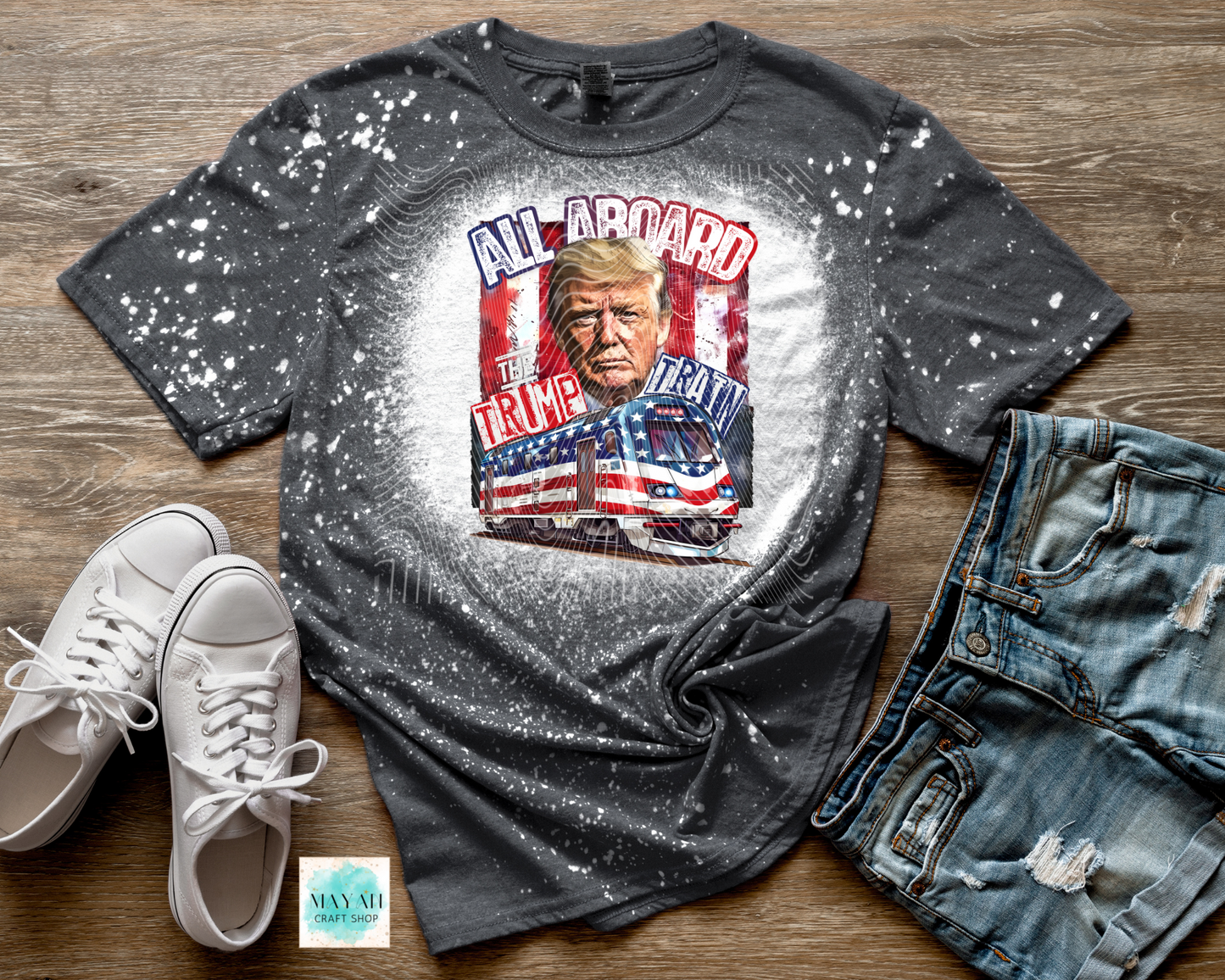 Gray t-shirt with graphic design featuring a face and text, paired with white sneakers and blue jeans on a wooden surface.