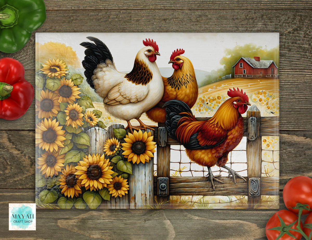 A cutting board featuring a colorful illustration of three chickens and sunflowers on a rustic wooden fence, shown on a dark wood background with decorative bell peppers and tomatoes around it.