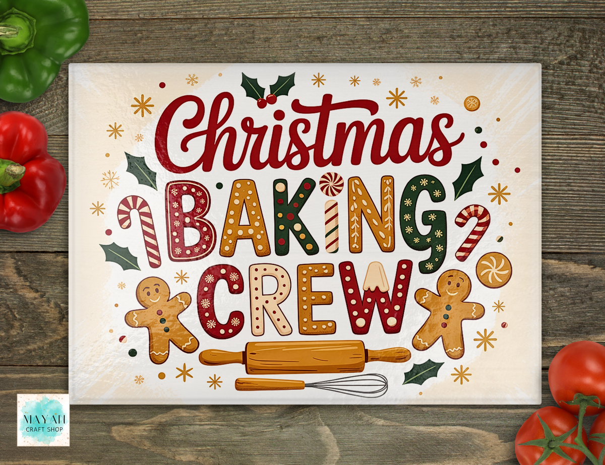 Acutting board with a festive Christmas baking theme, featuring the words 'Christmas Baking Crew' in decorative red, green, gold, and gingerbread-inspired lettering, surrounded by candy canes, holly, gingerbread men, and a rolling pin. The sign is photographed flat on a rustic wood surface with red bell peppers and tomatoes partially visible around it.