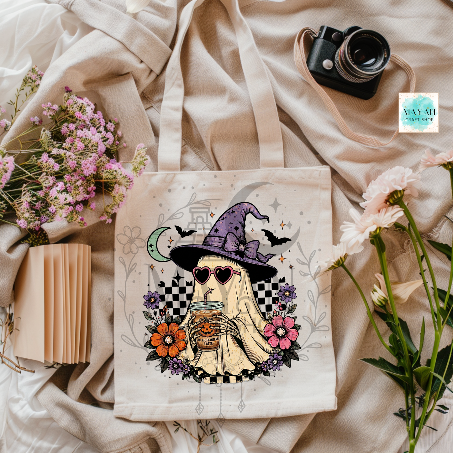 Tote bag with a Halloween-themed design featuring a ghost in a witch hat, surrounded by flowers and a camera on a fabric background.