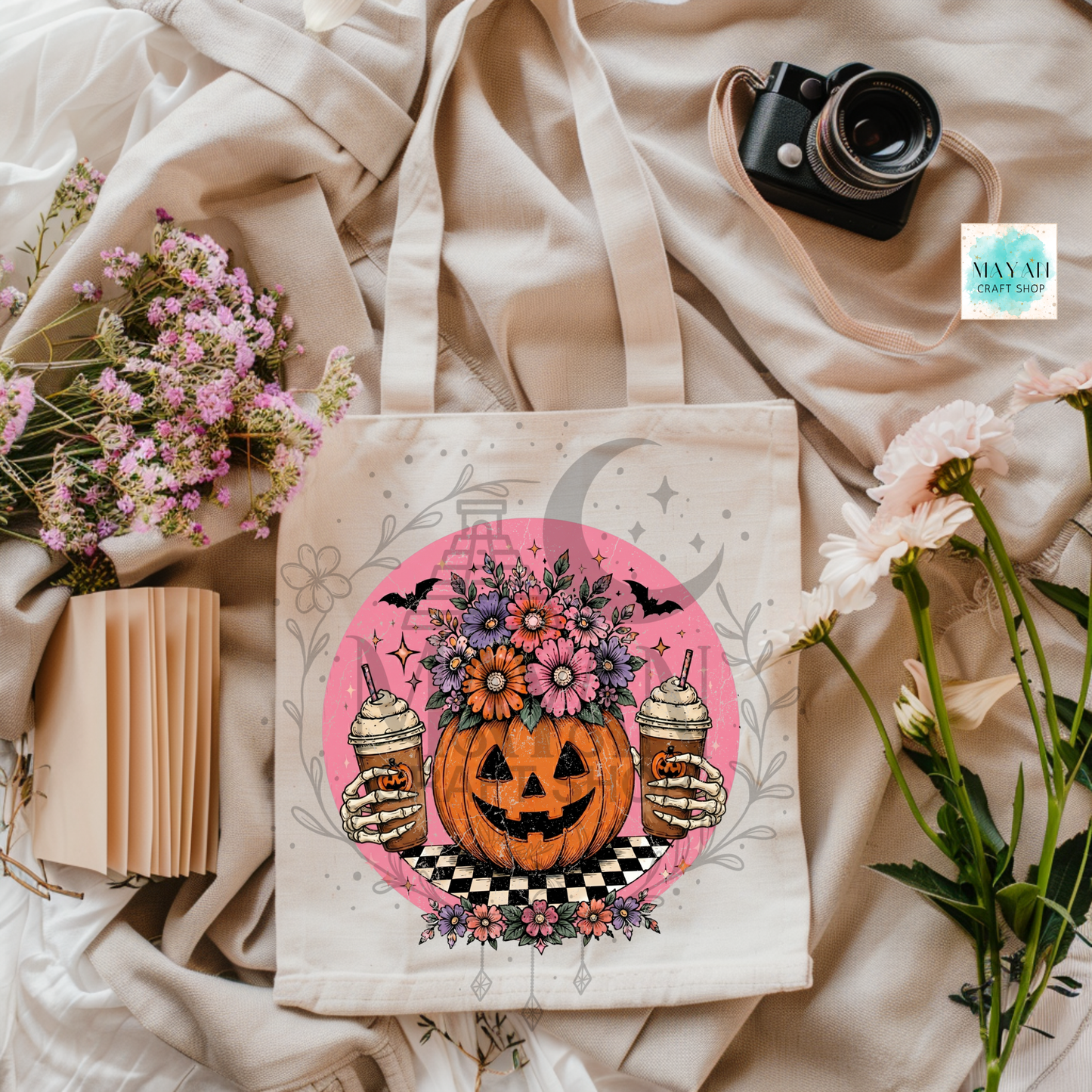 Tote bag with Halloween design featuring a pumpkin, flowers, and drinks on a beige fabric background.