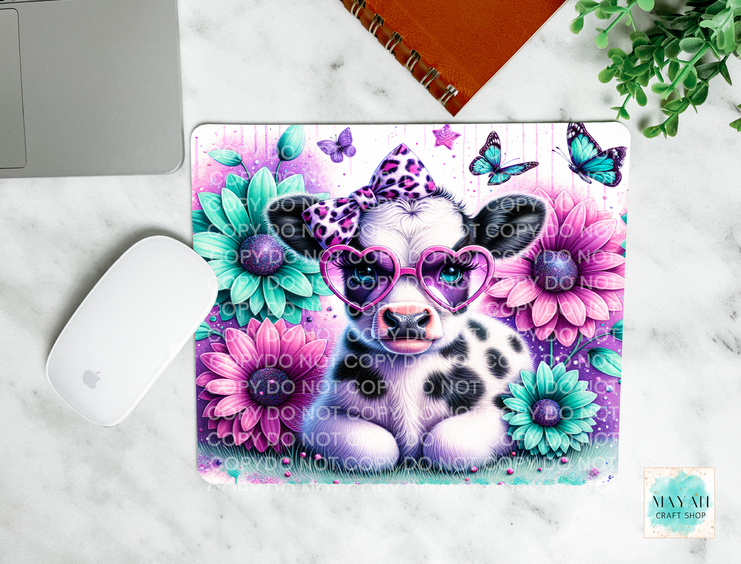 Colorful cow design with flowers and butterflies on a laptop case, placed on a marble surface.