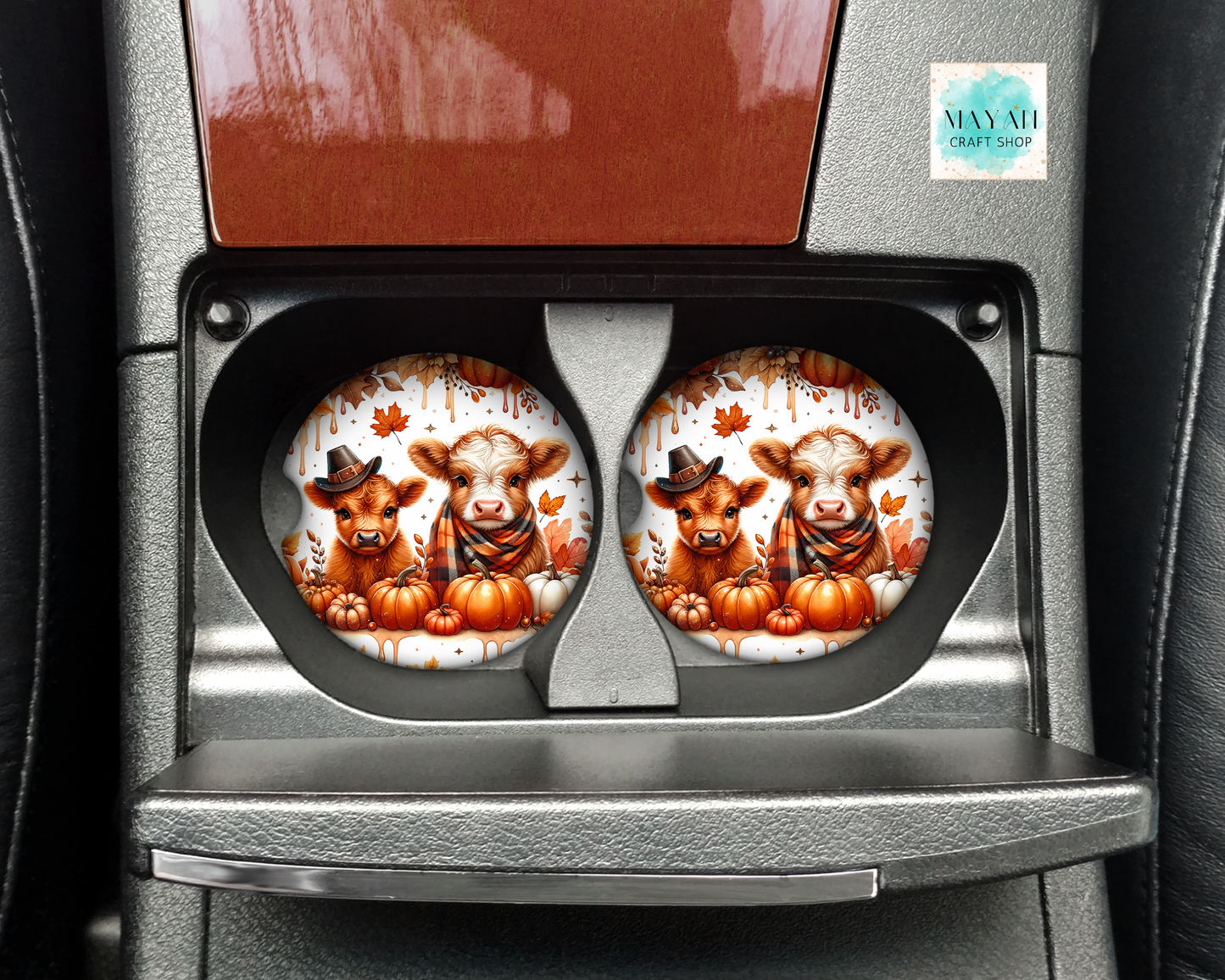 Two car coasters with cow and pumpkin design in a cup holder.