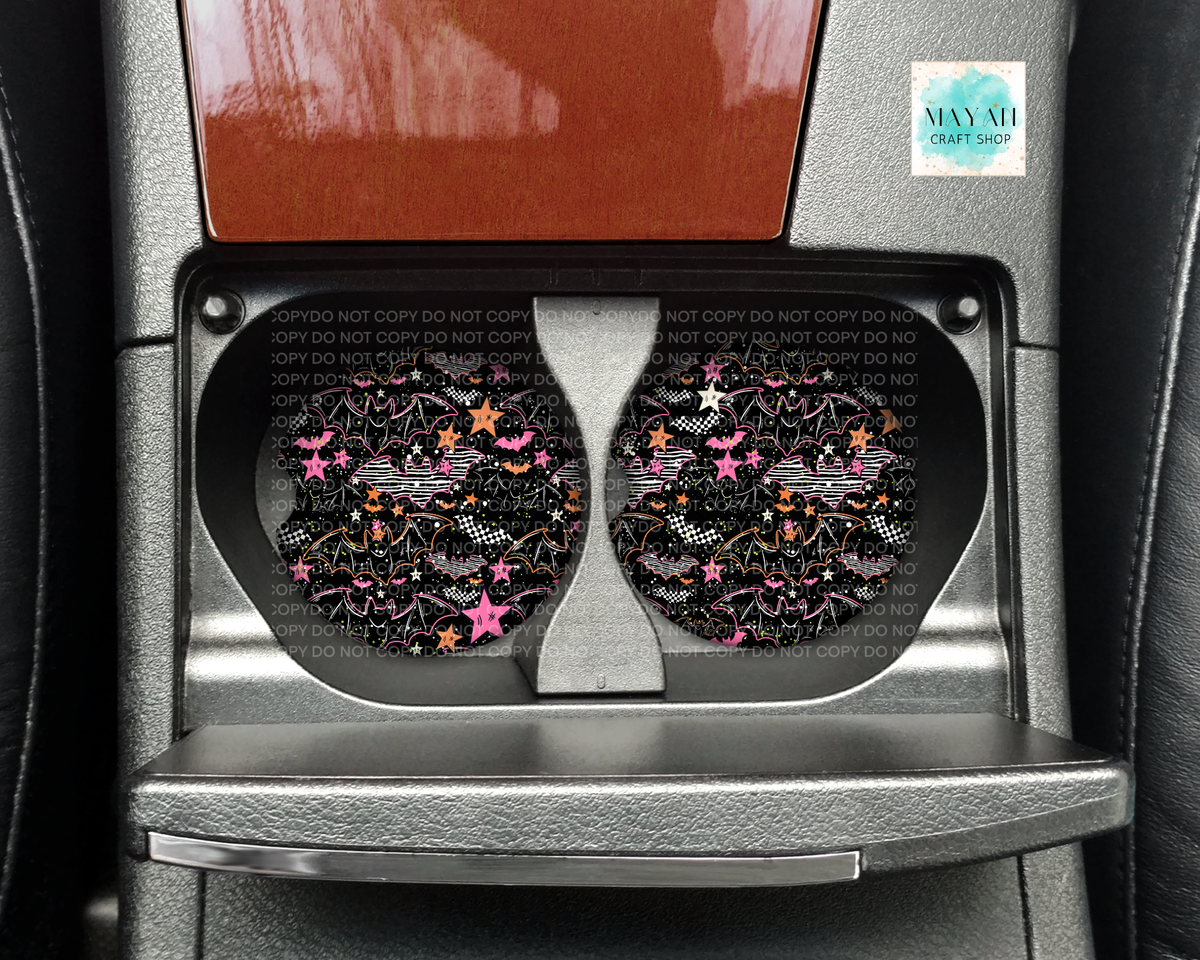 A pair of circular car cup holders installed in a center console, featuring a black background with a colorful pattern of stars, glitter, and checkered flags. The cup holders are set against a car interior with a brown wood trim panel above.