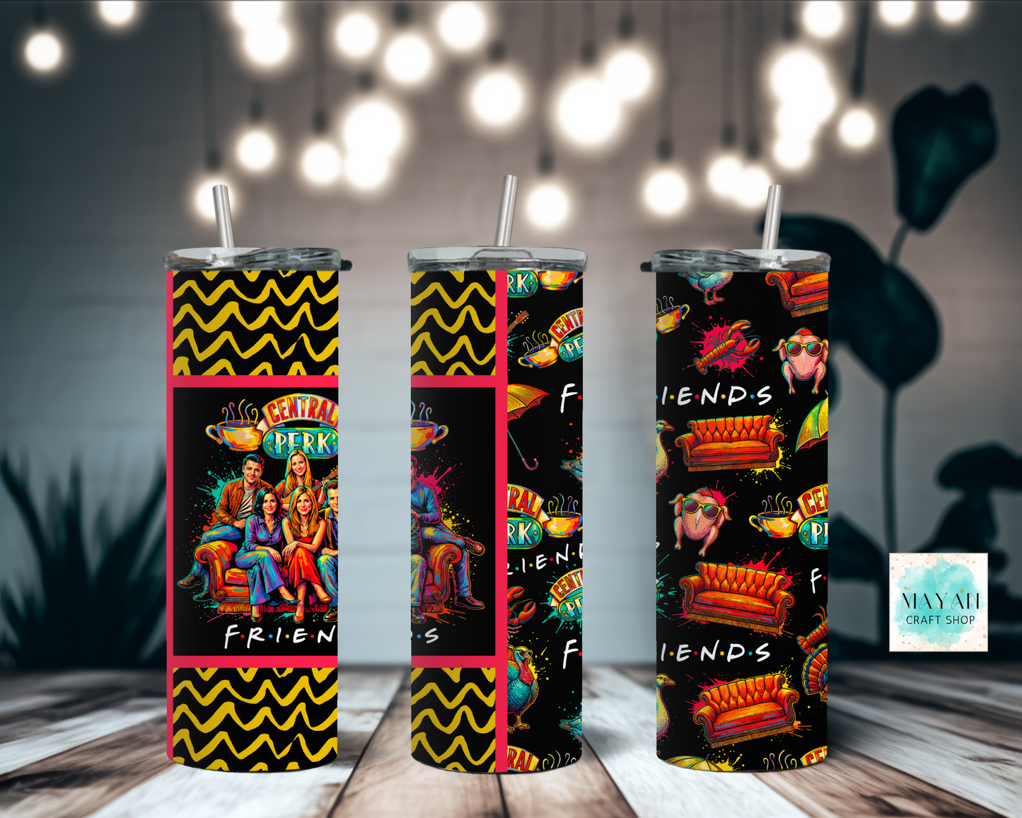 Three tumblers with tv show themed designs on a wooden surface with blurred lights in the background.