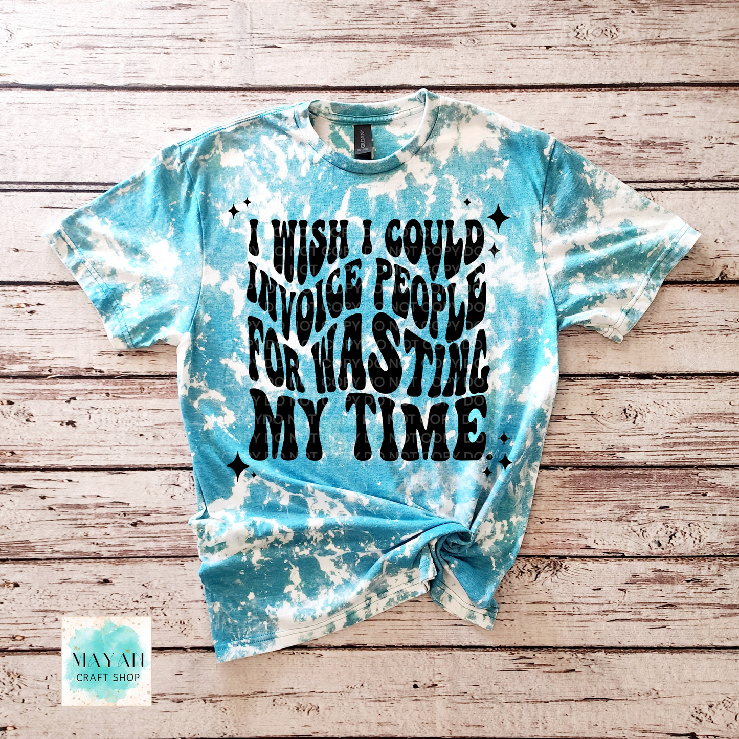 Blue tie-dye t-shirt with text on a wooden surface, featuring the brand 'Mayan Craft Shop'.