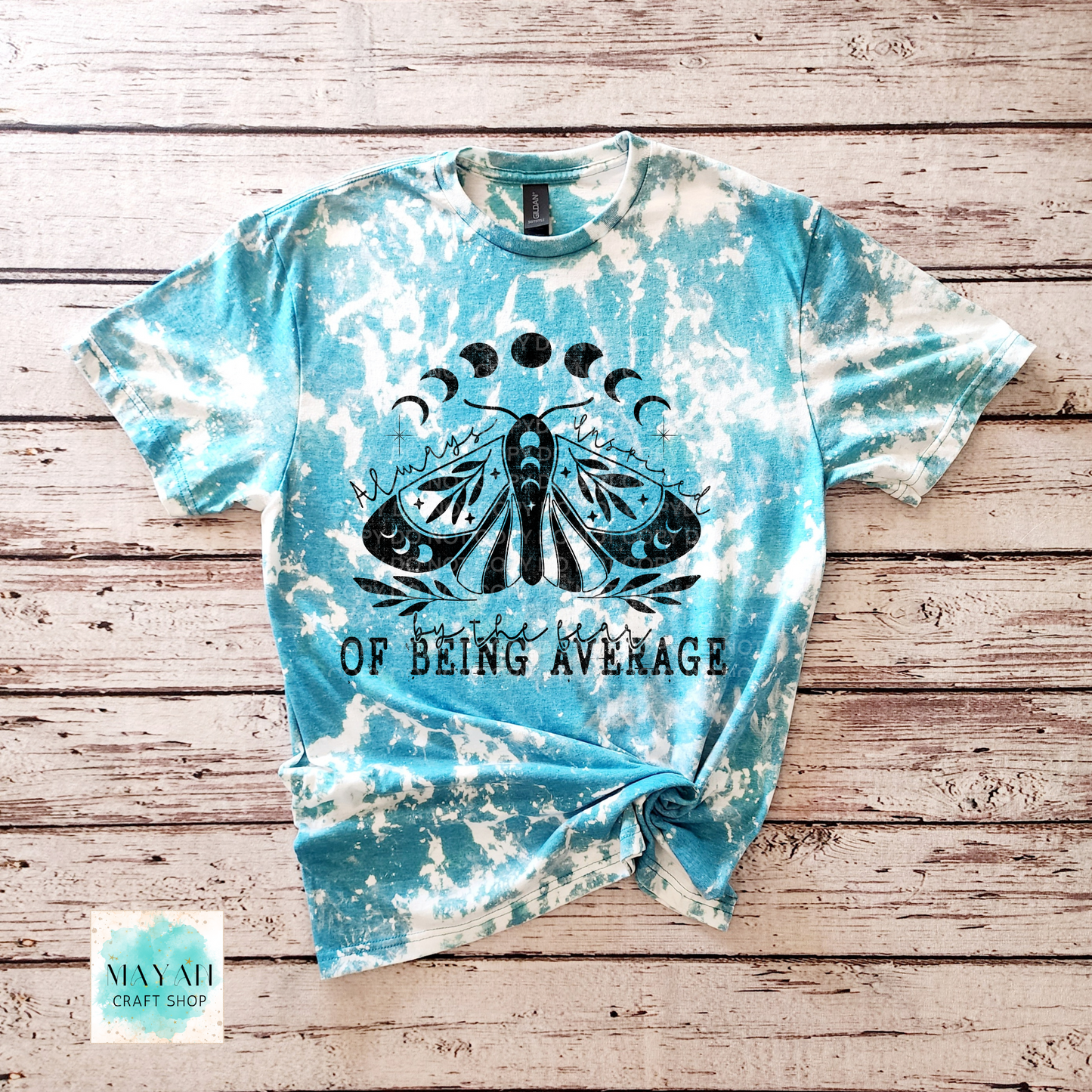 Tie-dye t-shirt with a black moth graphic and text on a wooden surface, featuring the brand 'Mayan Craft Shop'.