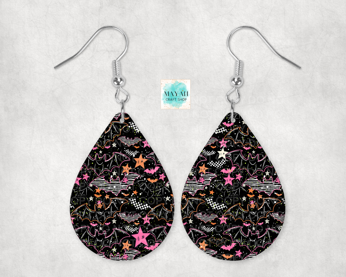 A pair of teardrop-shaped dangle earrings with a black background and a colorful pattern of pink stars, orange stars, white stars, and whimsical doodles. The earrings are suspended from silver fishhook wires.