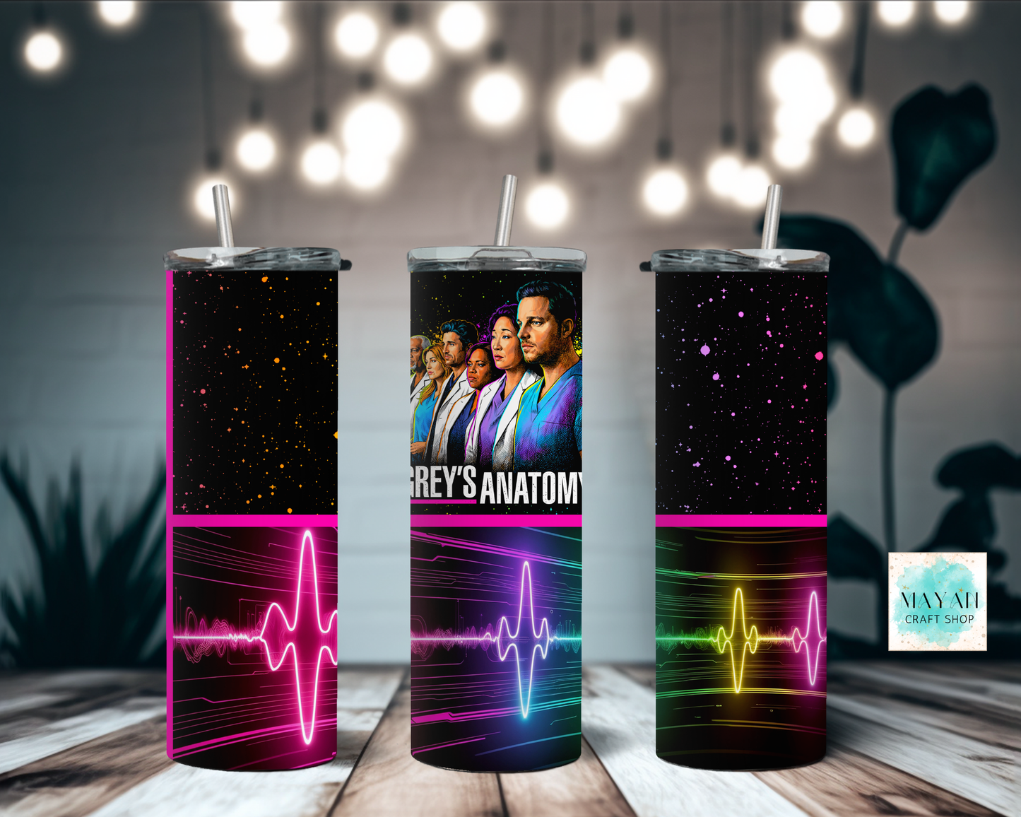 Three tumblers with tv show design on a wooden surface with blurred lights in the background.