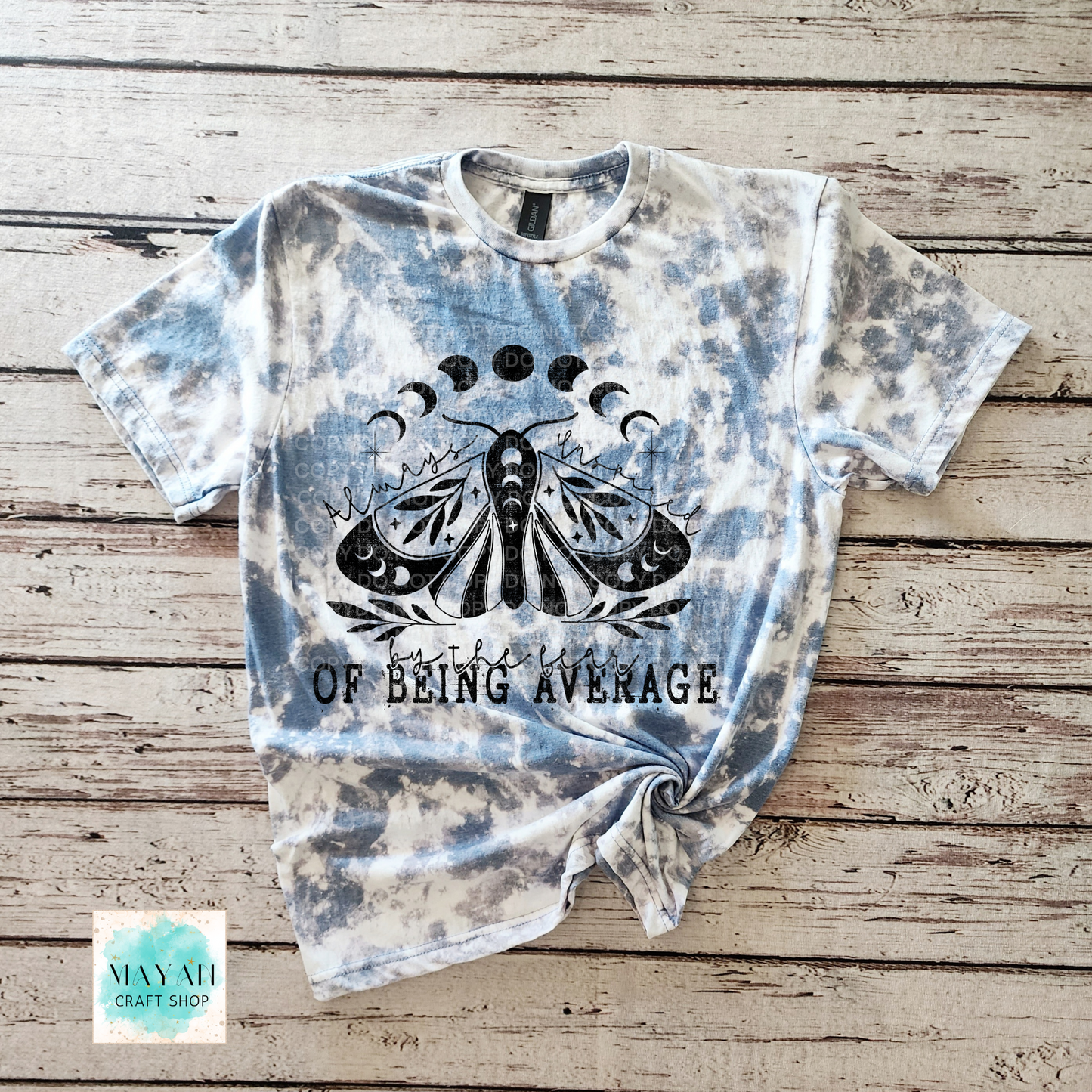 Tie-dye t-shirt with a moth graphic and text on a wooden surface, featuring the brand 'Mayan Craft Shop'.