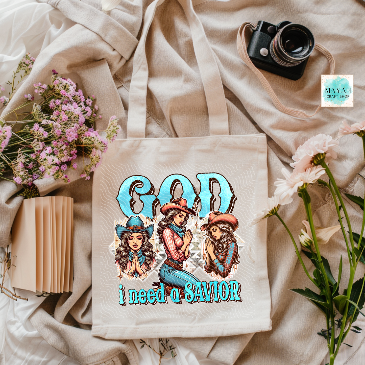Tote bag with graphic design featuring three women in cowboy hats and text 'God I need a SAVIOR' on a soft fabric background.