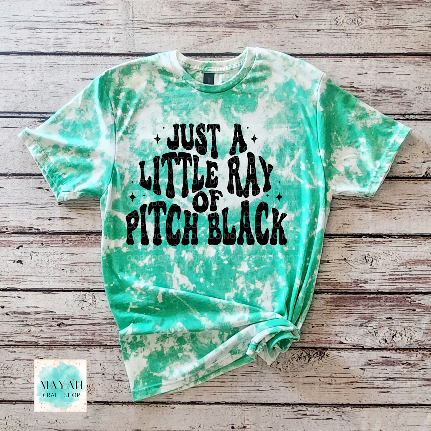 Green tie-dye t-shirt with black text on a wooden surface, featuring the brand 'Mayan Craft Shop'.