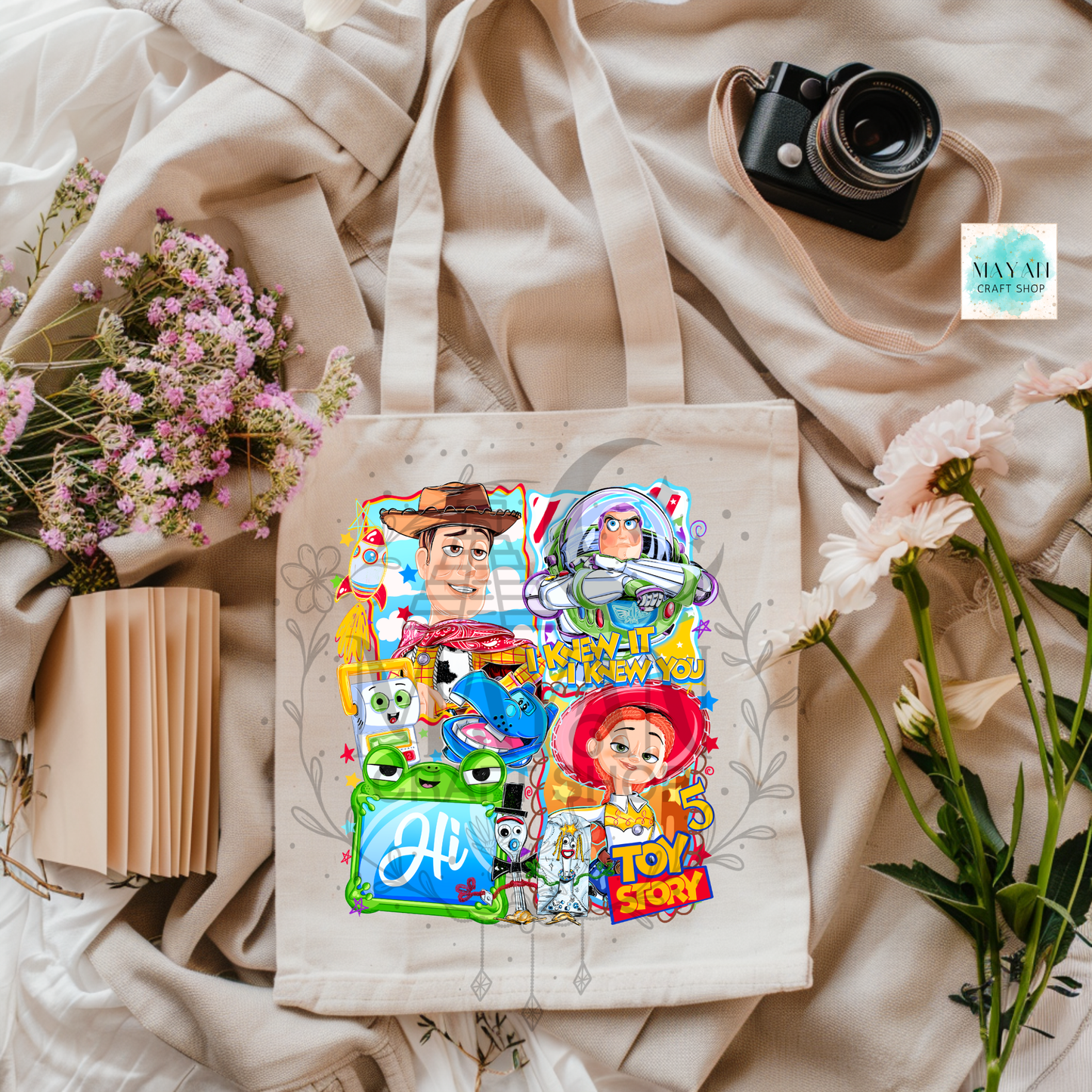 Tote bag with character designs on a beige fabric background with flowers and a camera.