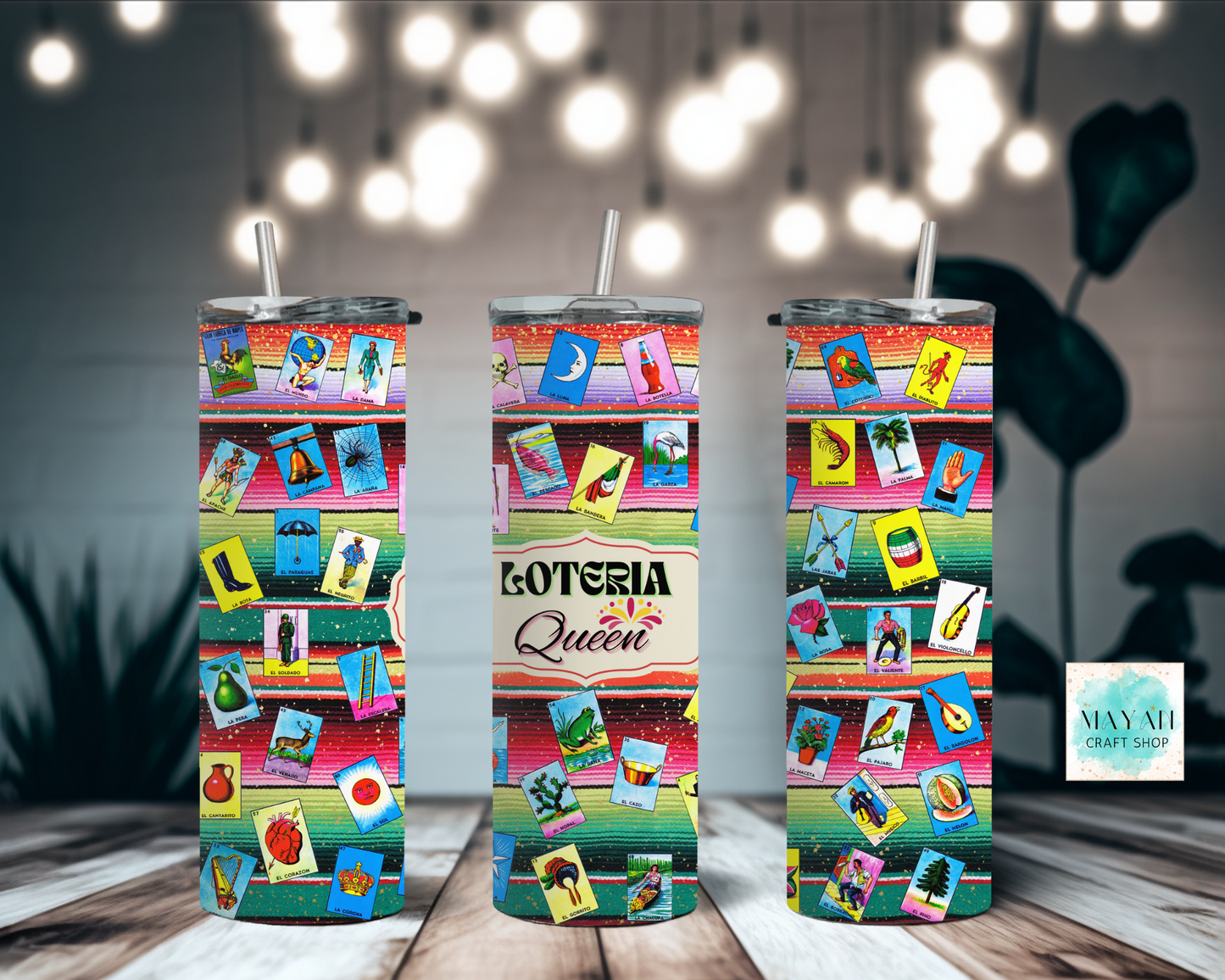 Three colorful tumblers with 'Loteria Queen' design on a wooden surface with blurred lights in the background.