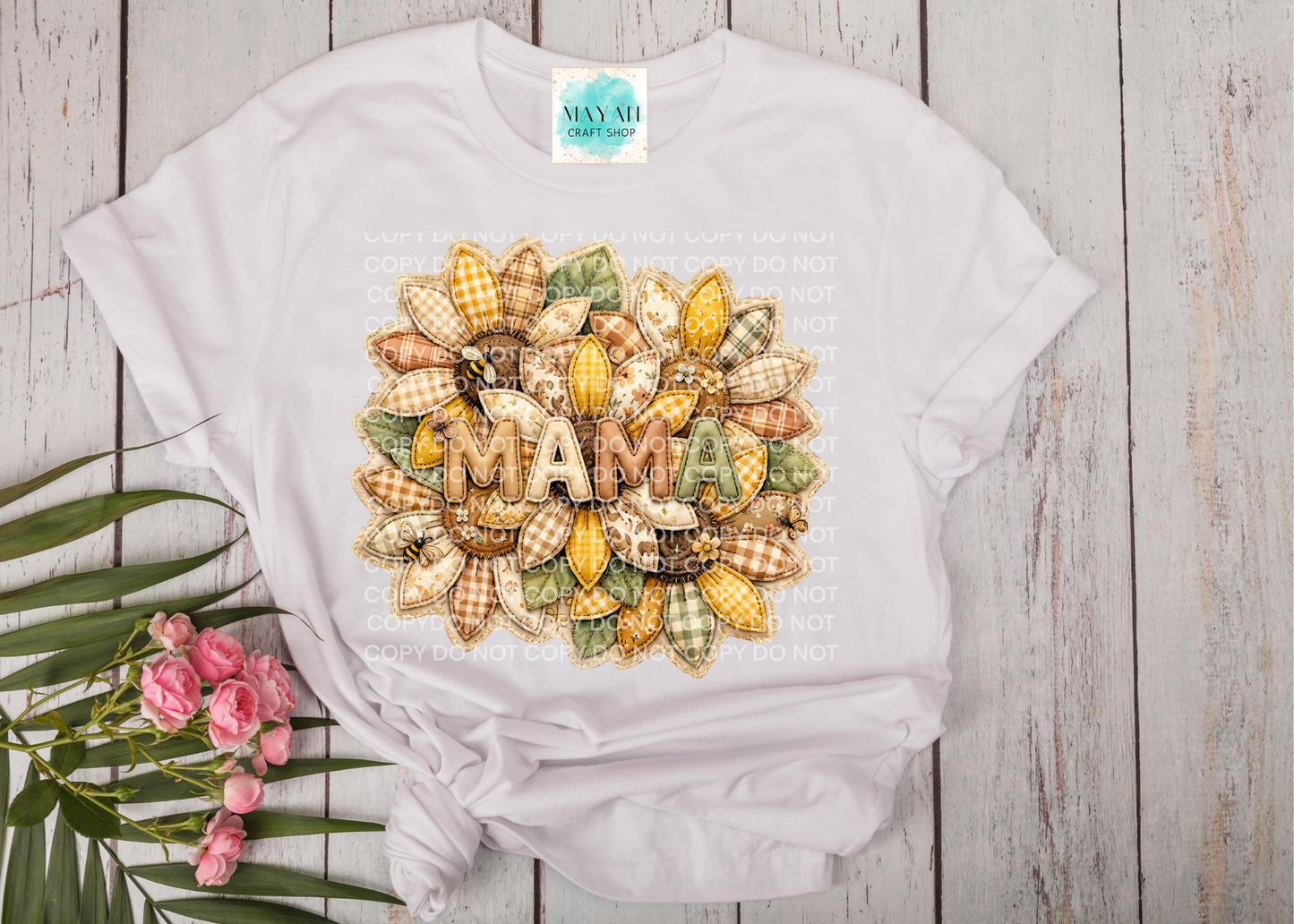 White t-shirt with decorative 'MAMA' design on a wooden surface with flowers.