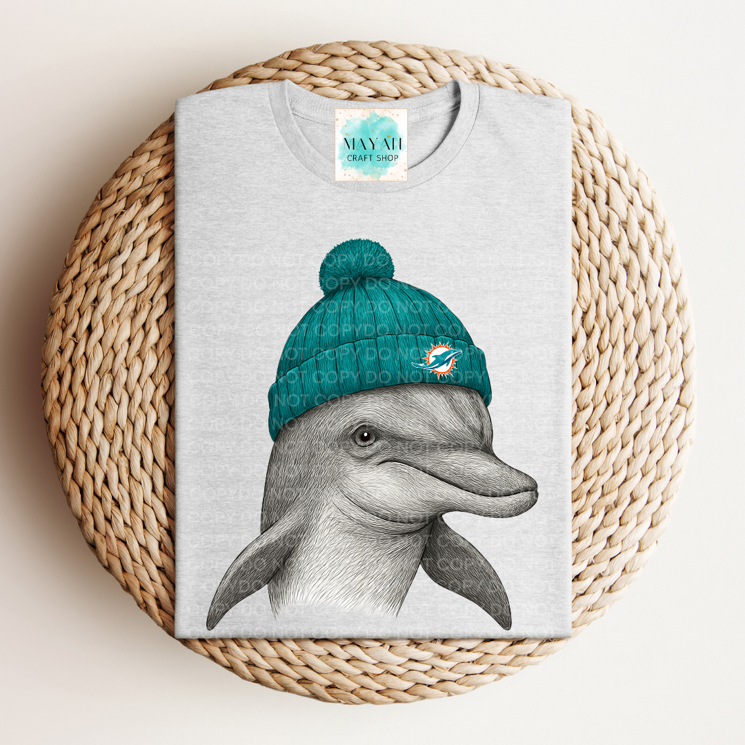 Gray t-shirt with a dolphin wearing a teal beanie on a woven surface