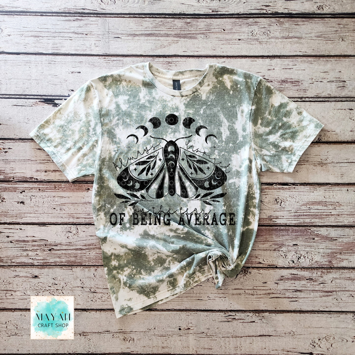 Dye-sublimated t-shirt with a moth design and text on a wooden surface, featuring the brand 'Mayan Craft Shop'.
