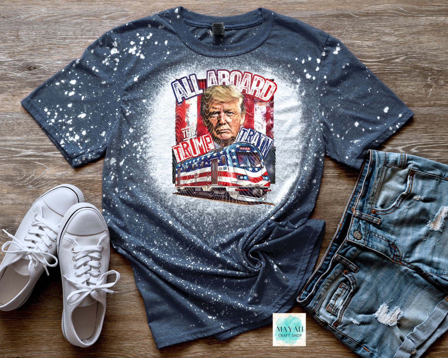 Blue graphic t-shirt with a printed design, white sneakers, and jeans on a wooden surface.