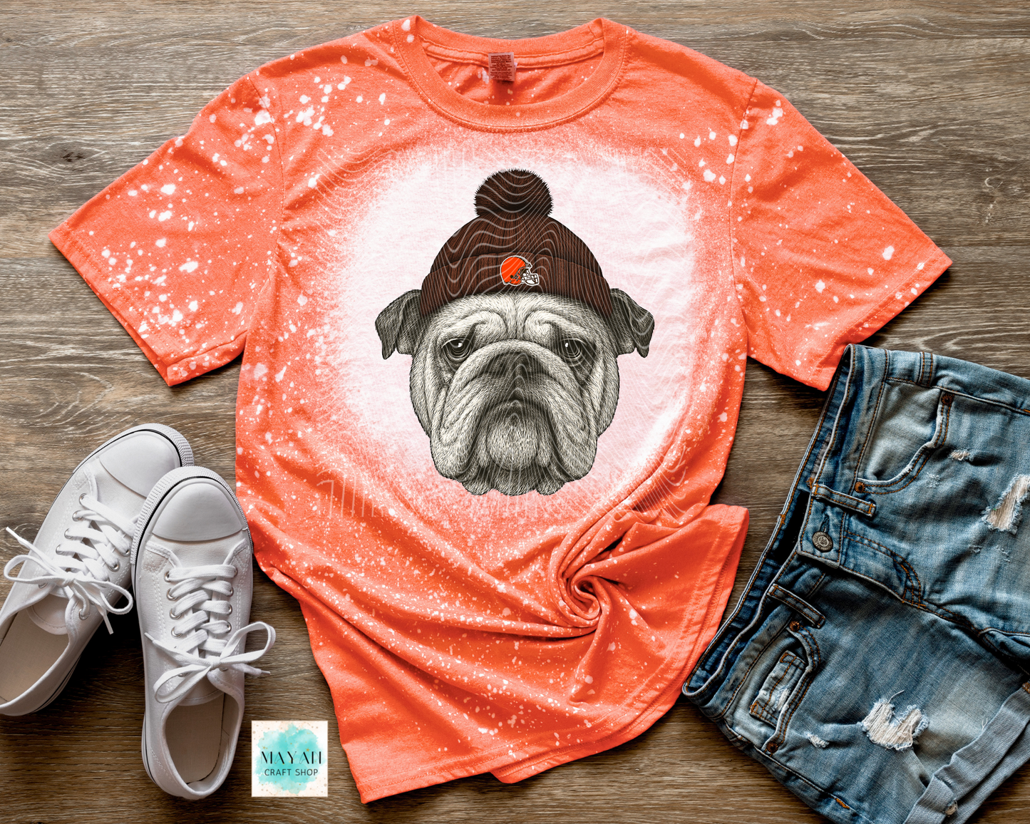 Orange t-shirt with a dog graphic, white sneakers, and denim shorts on a wooden surface.
