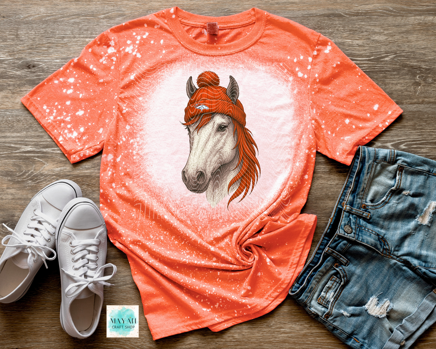 Orange t-shirt with horse graphic, white sneakers, and denim shorts on a wooden surface