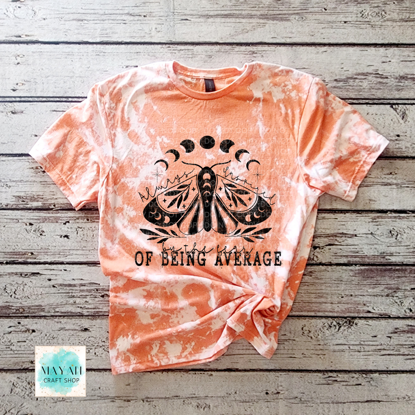 Tie-dye t-shirt with a black moth graphic and text on a wooden surface, featuring the brand 'Mayan Craft Shop'.