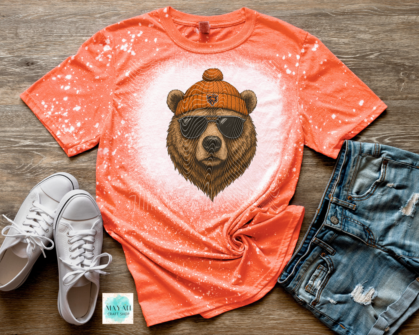 Orange t-shirt with bear graphic, white sneakers, and denim shorts on a wooden surface