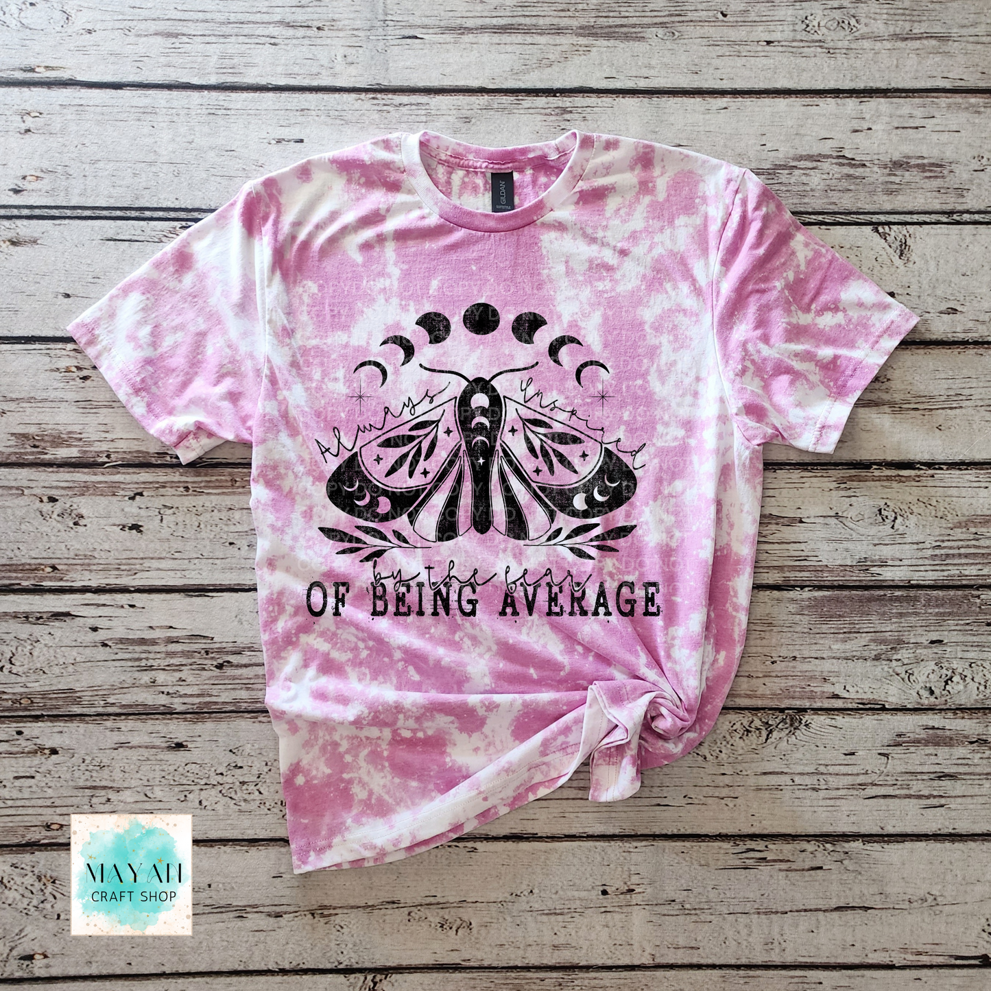 Pink tie-dye t-shirt with a black butterfly graphic and text on a wooden surface, branded 'Mayan Craft Shop'.