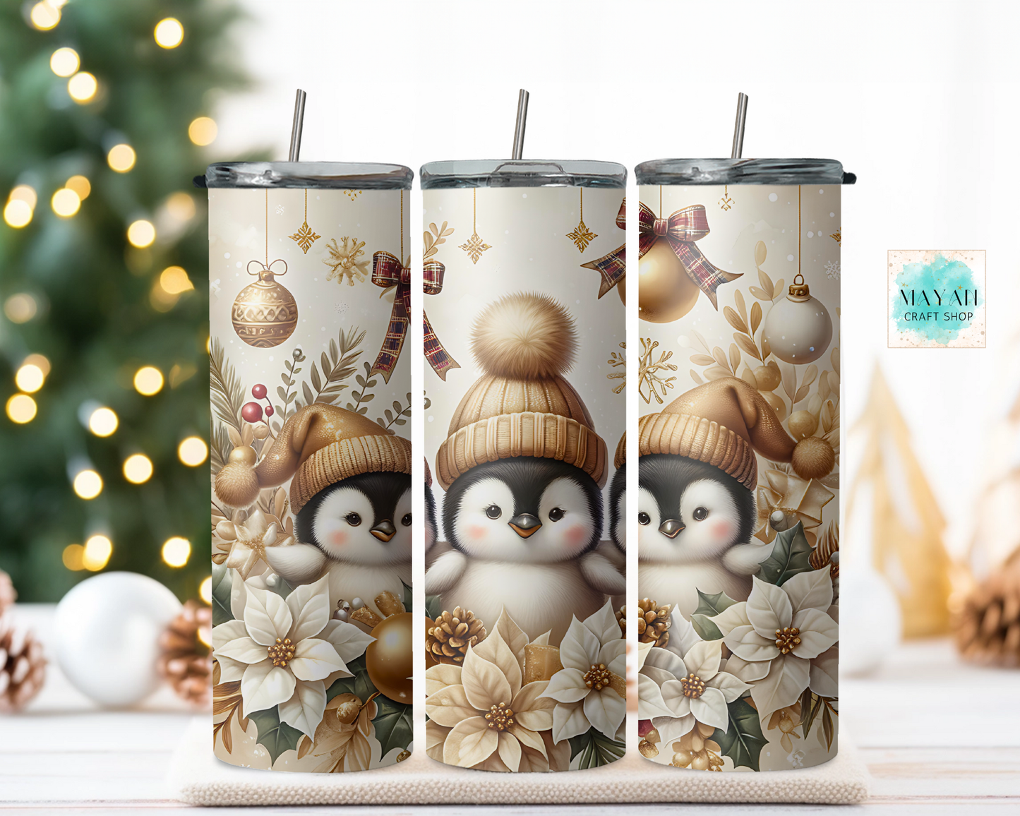 Three tumblers with penguin design and Christmas elements on a wooden surface with a blurred Christmas tree background.