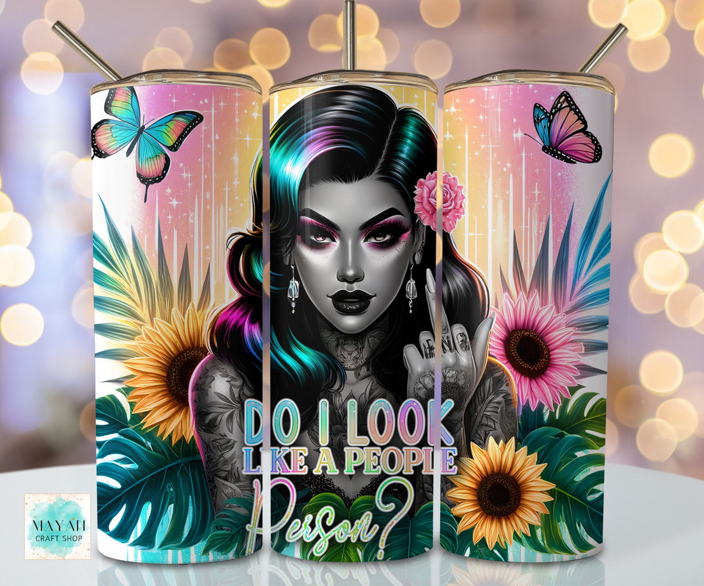 Three tumblers with a colorful design featuring a person with tattoos, flowers, and butterflies on a blurred bokeh background.