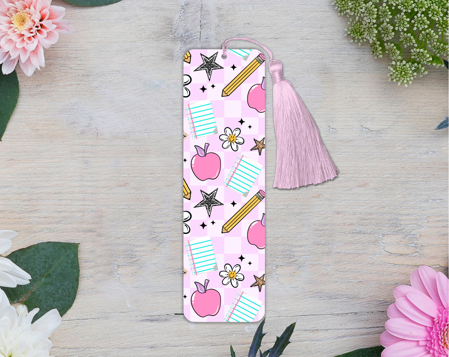 Pink bookmark with tassel on a wooden surface with flowers