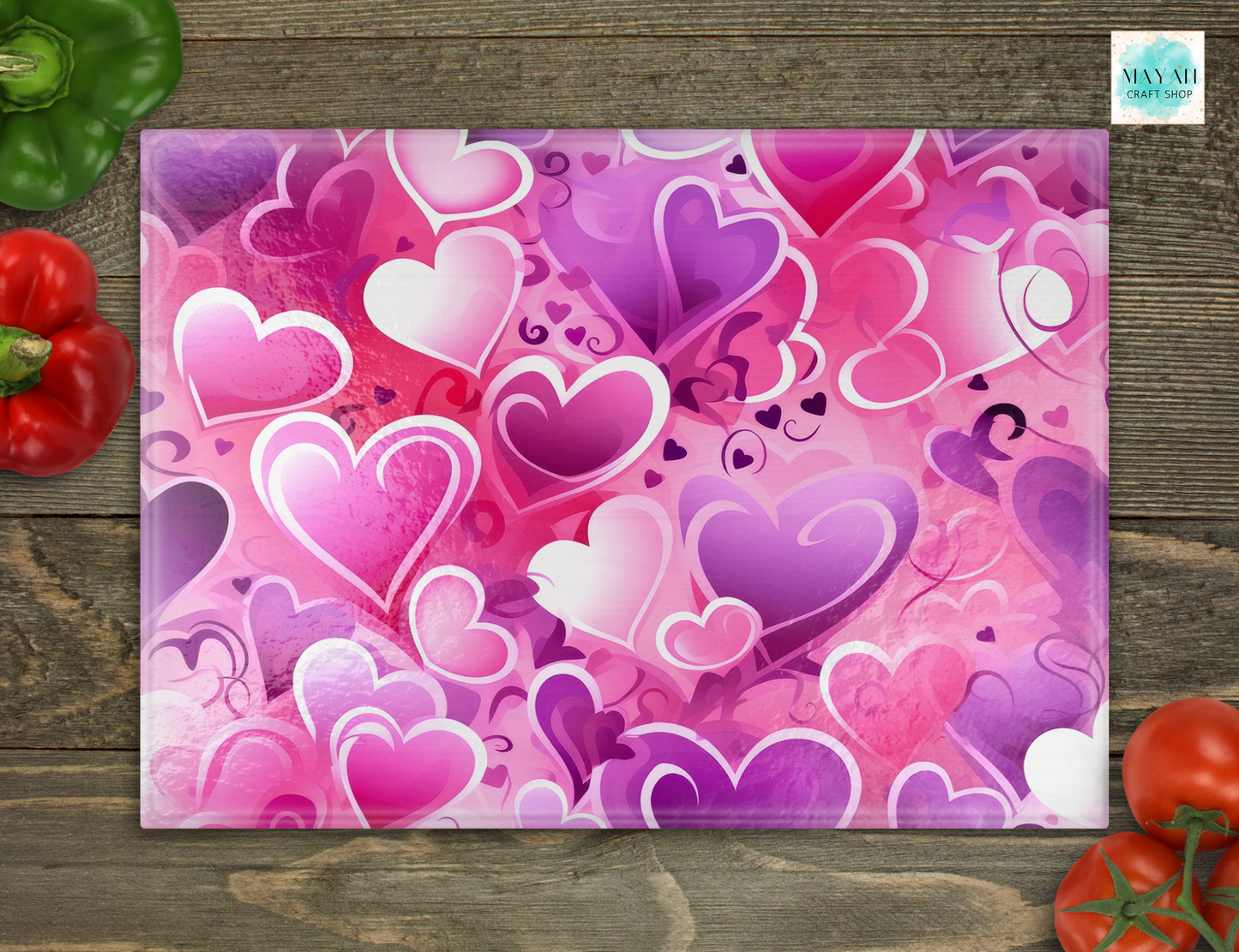 Pink and purple heart-patterned cutting board on a wooden surface with vegetables.