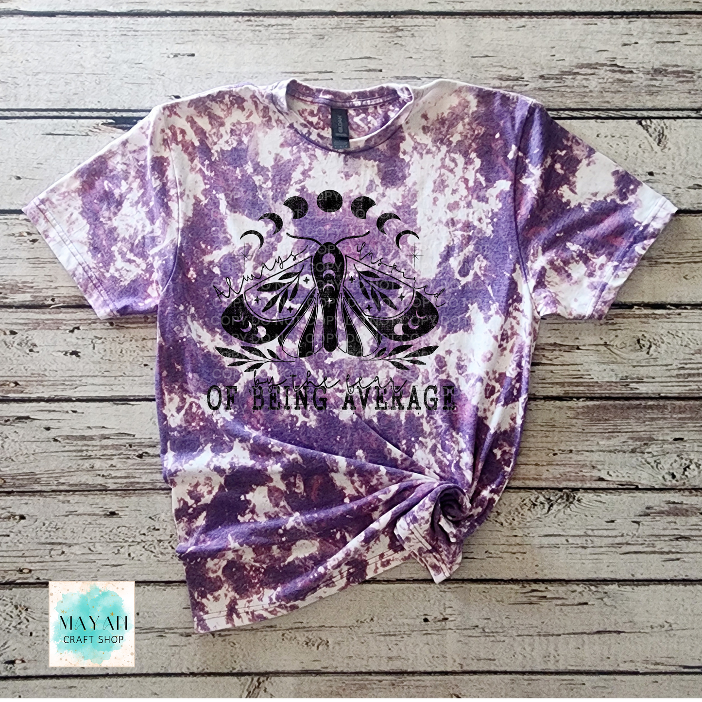 Purple tie-dye t-shirt with a black graphic and text on a wooden surface, featuring the brand 'Mayan Craft Shop'.