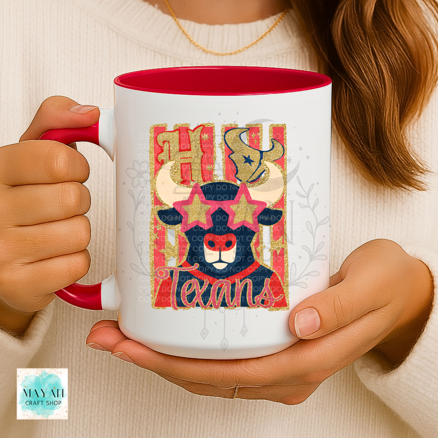 A person holds a white ceramic mug with a red interior and handle. The mug features a colorful graphic of a Texas horned animal mascot with a word and a gold glittery 'H' above it.