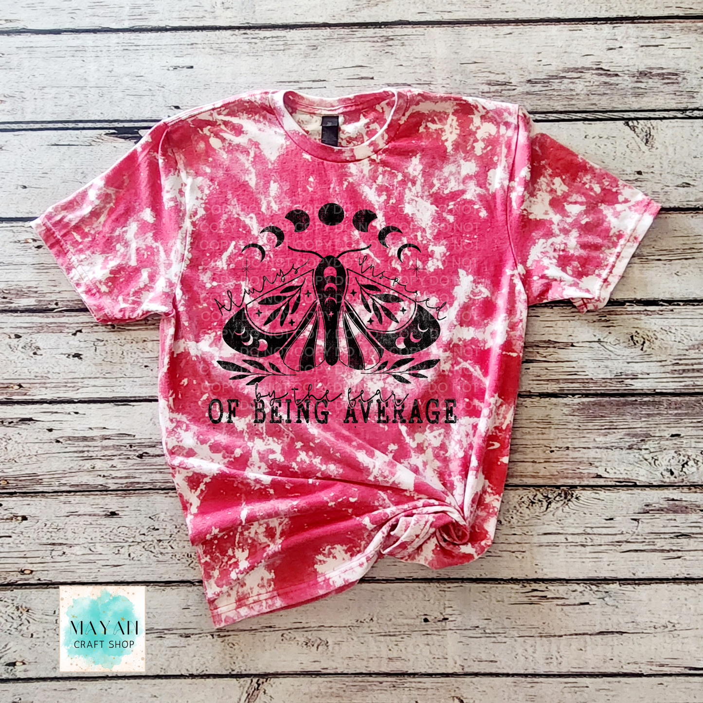 Pink tie-dye t-shirt with black graphic and text on a wooden surface, brand 'Mayan Craft Shop'.