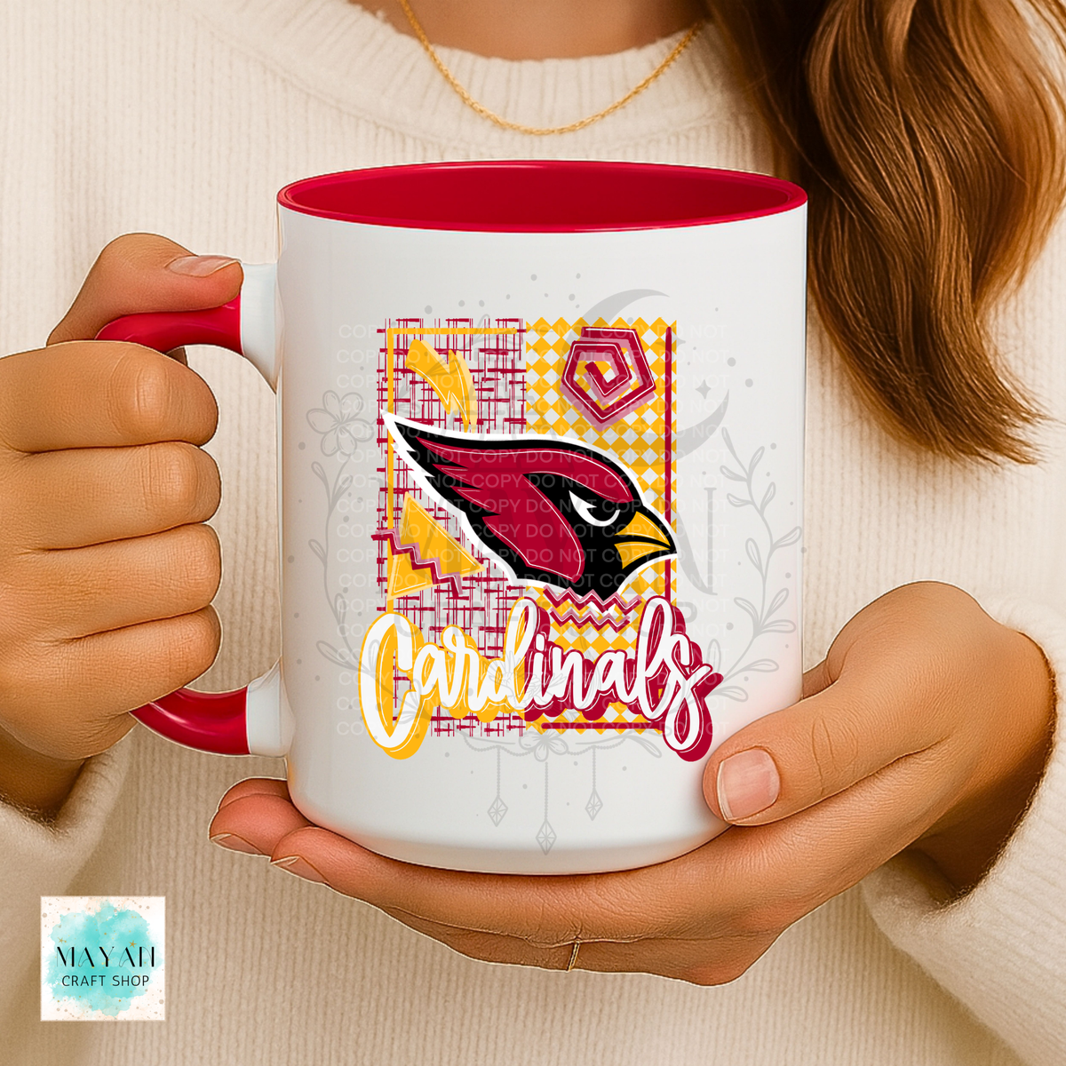 A person holds a white ceramic mug with a red interior and handle. The mug features a colorful team logo and a word in script.