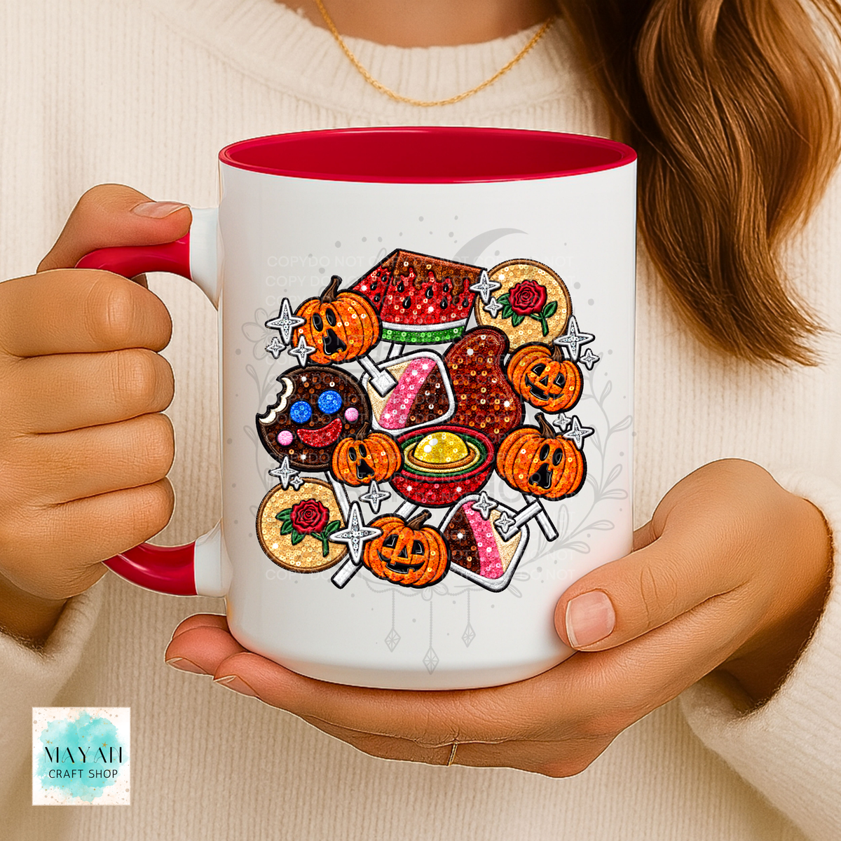 A person holding a white ceramic mug with a red interior and handle, featuring a colorful Halloween-themed graphic of mexican candy. The person is wearing a cream knit sweater.