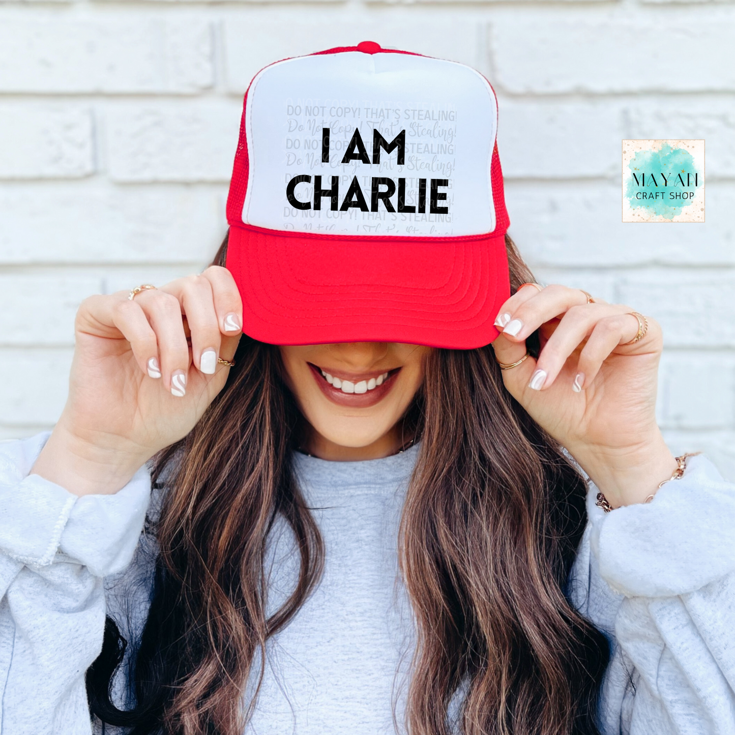 Person holding a red and white cap with 'I am Charlie' text against a light brick wall.