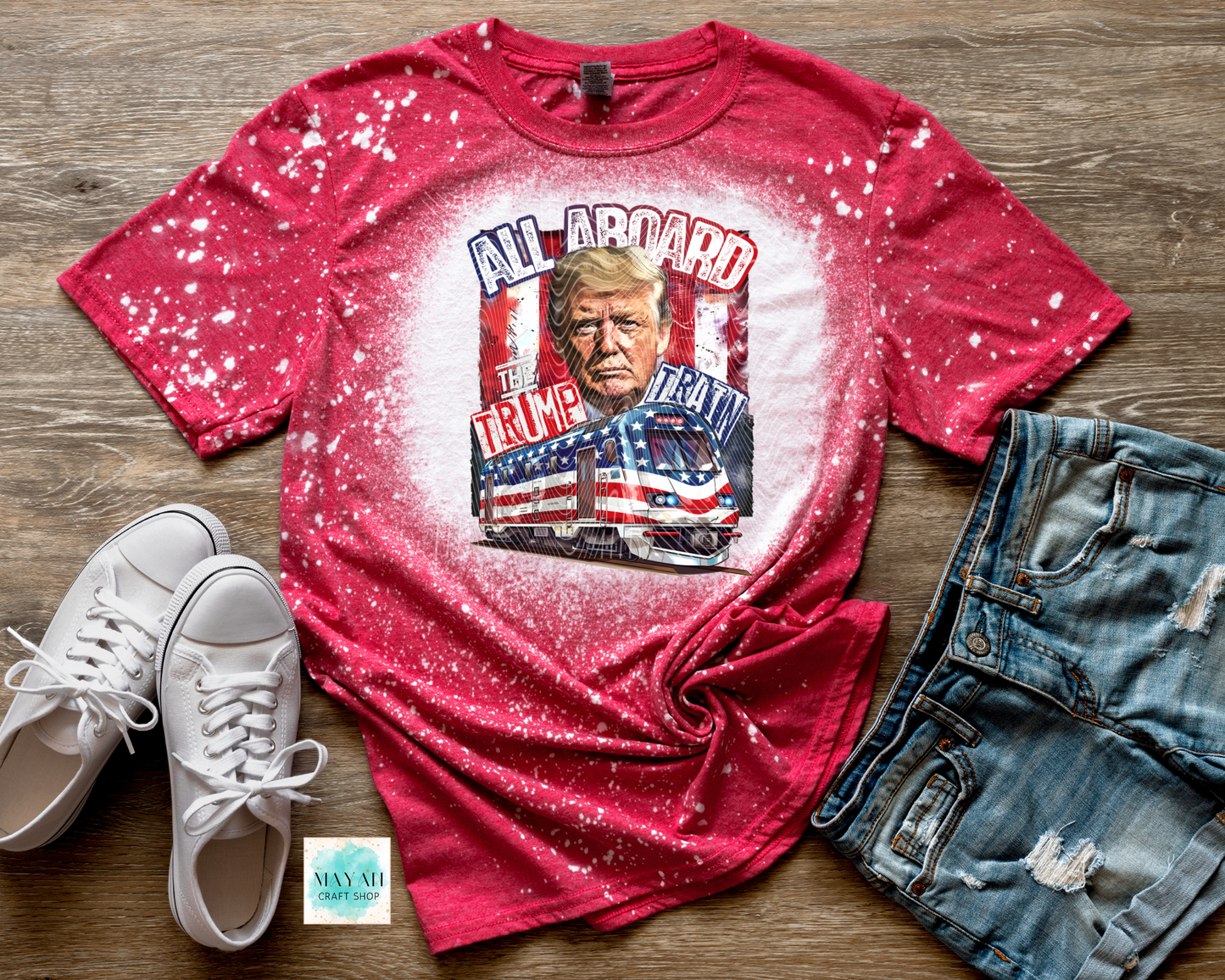 Red t-shirt with graphic design on a wooden surface with white sneakers and blue jeans.