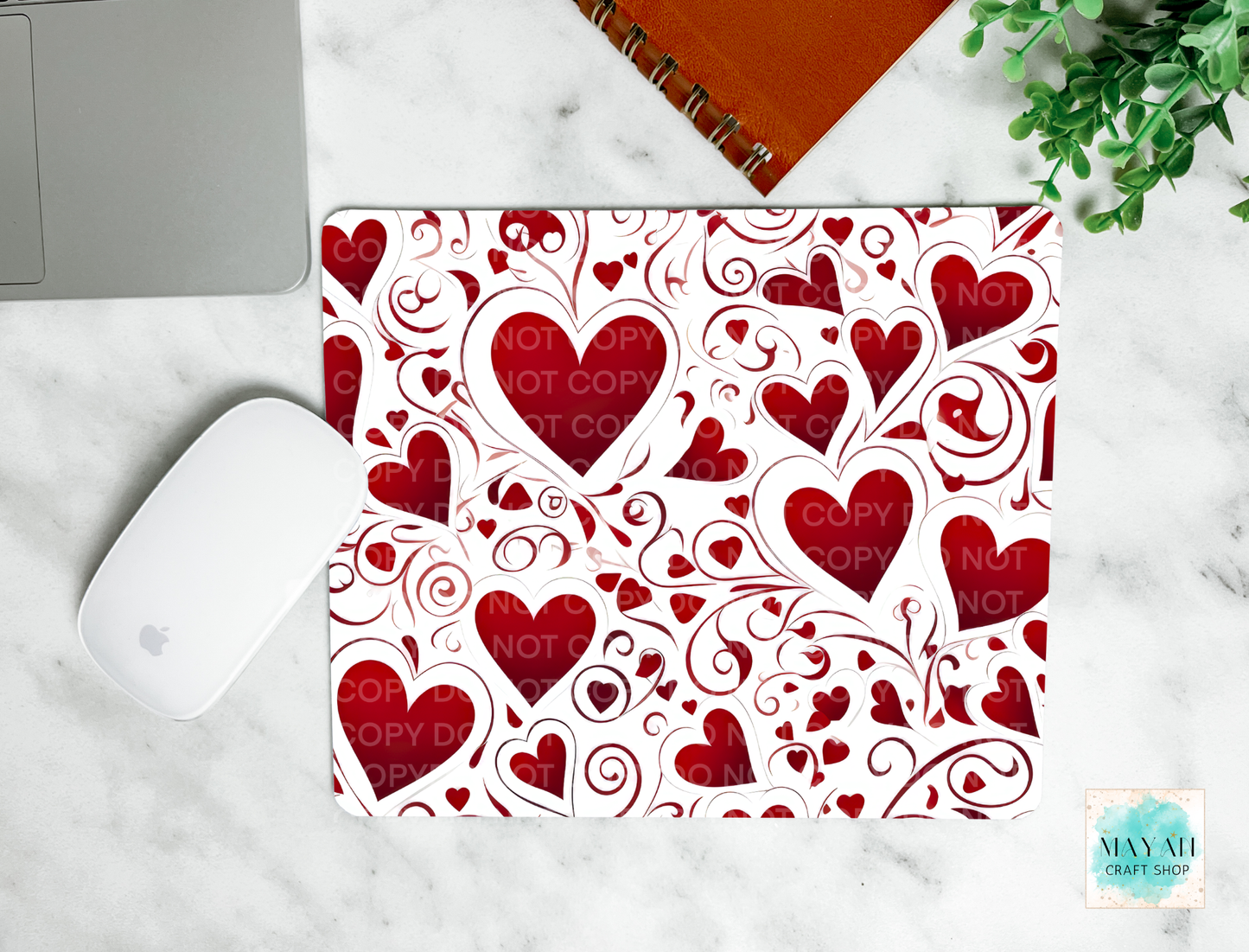 Heart patterned mouse pad on a marble surface with a laptop and mouse.